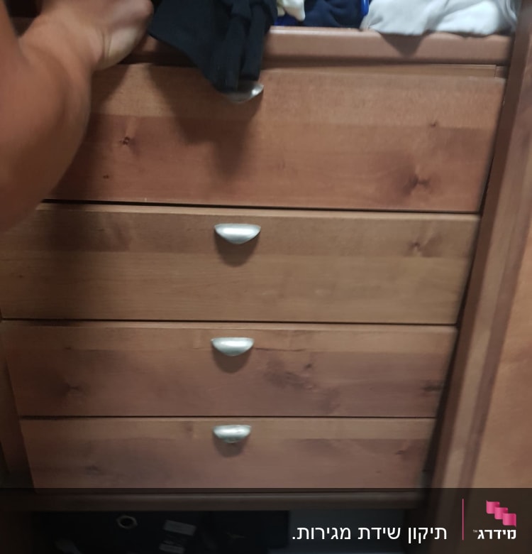 יד פותחת מגירת עץ בארון בגדים